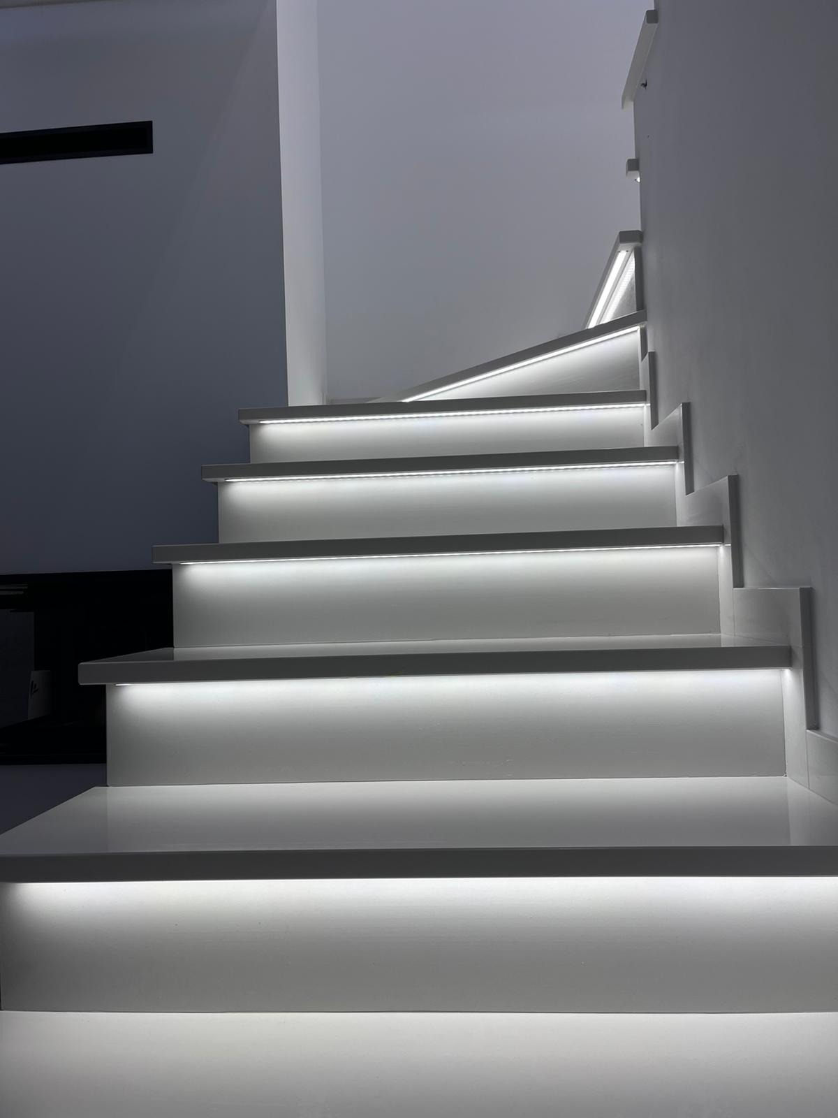 Nowoczesne, białe schody wewnętrzne z subtelnym podświetleniem LED pod każdym stopniem, tworzącym efektowną iluminację w minimalistycznym wnętrzu.