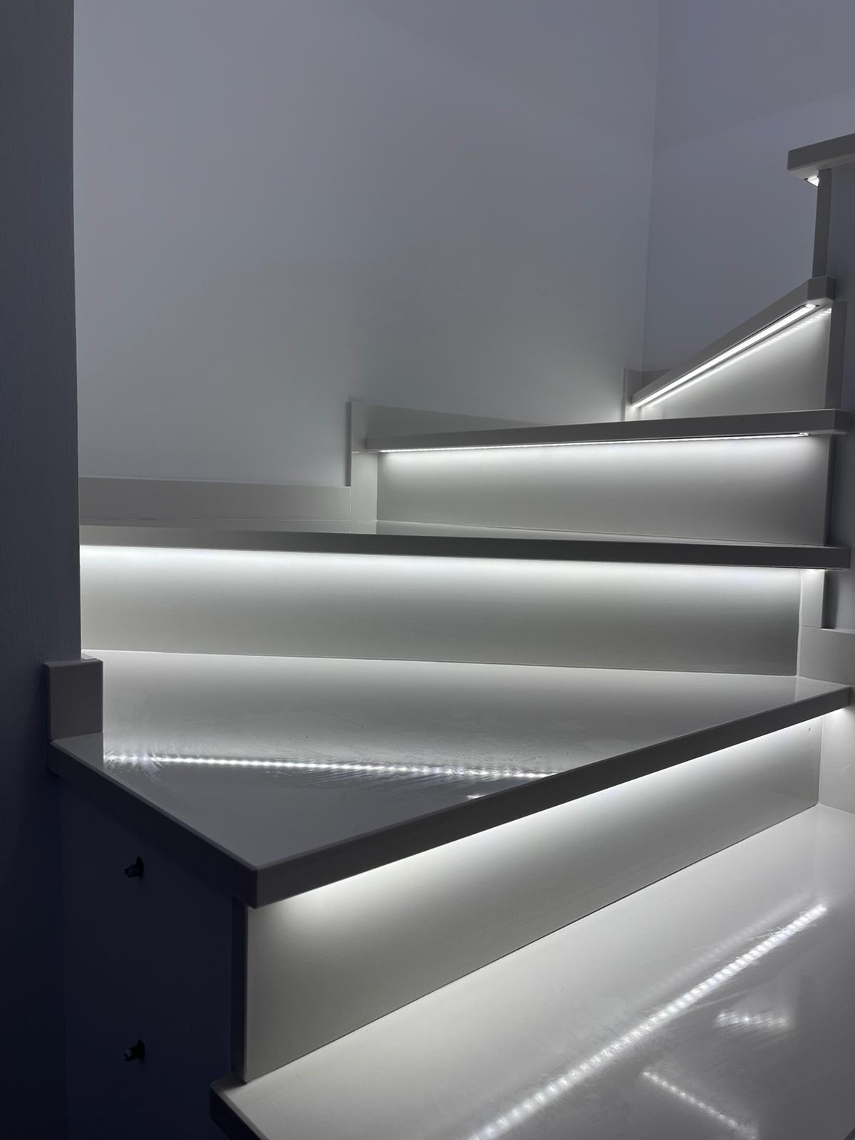 Nowoczesne, białe schody z podświetleniem LED na każdym stopniu, widok z dołu, minimalistyczny design.