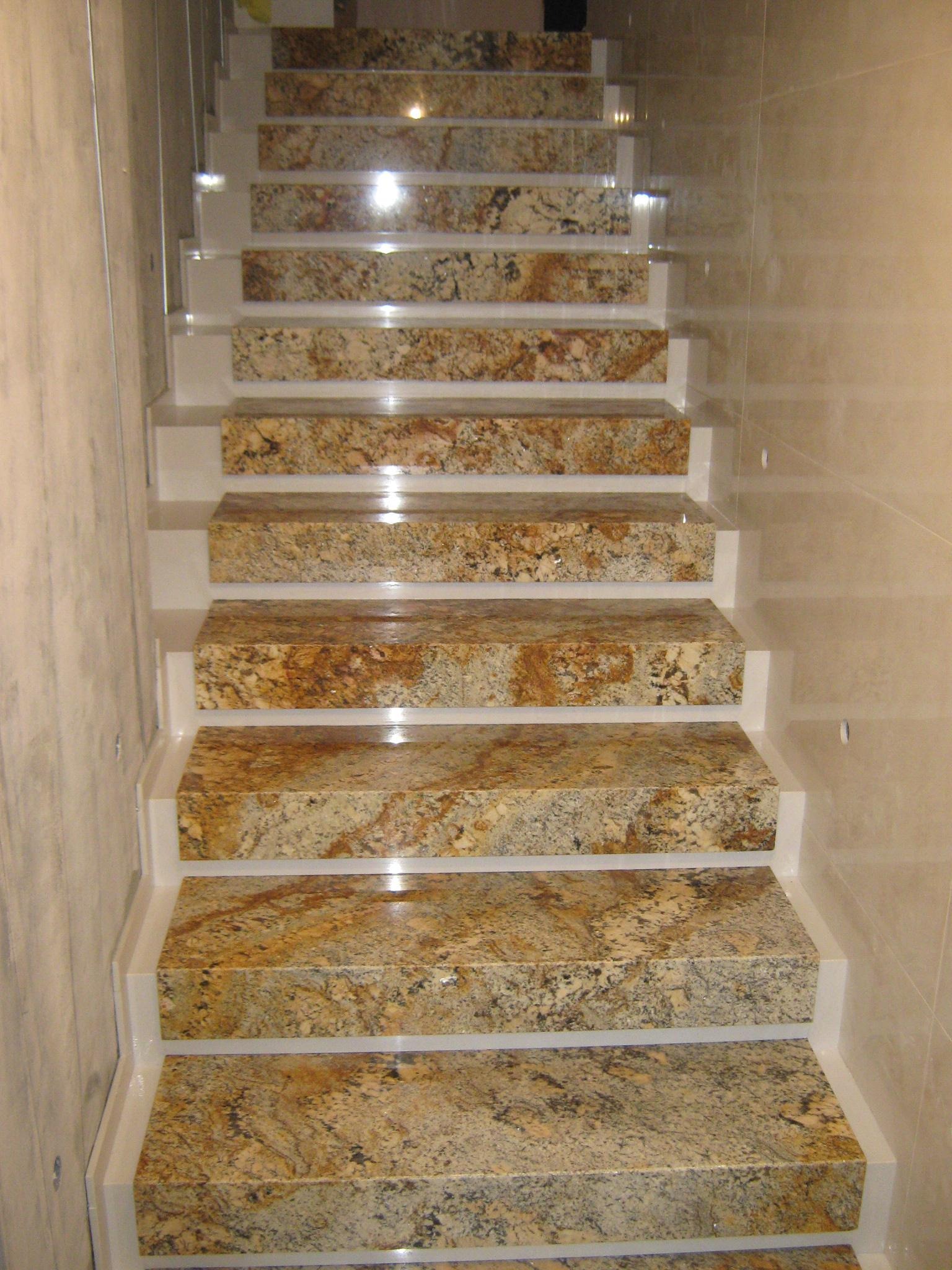 Wewnętrzne schody z polerowanego granitu w odcieniach beżu i brązu, osadzone w białej ramie, z błyszczącymi płytkami na ścianie w tle.