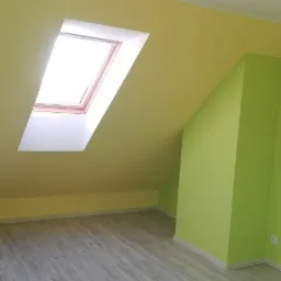 Pomalowane poddasze ze skośnym sufitem i oknem dachowym, ściany w dwóch odcieniach zieleni i żółci, panele podłogowe w odcieniach szarości.
