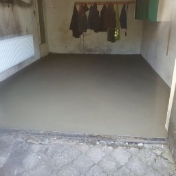 LUX-MIX ARTUR KIJAK - Świeżo wylana, gładka posadzka jastrychowa w garażu z grzejnikiem na ścianie i wiszącymi ubraniami.