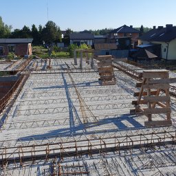 LUX-MIX ARTUR KIJAK - Zbrojenie stropu budynku jednorodzinnego z widocznymi podporami szalunkowymi, przygotowane do zalania betonem, w tle zabudowa mieszkalna.