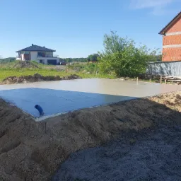 Wylana, świeża płyta betonowa fundamentowa pod budowę domu jednorodzinnego, widoczny niebieski przewód instalacyjny i otaczający grunt.