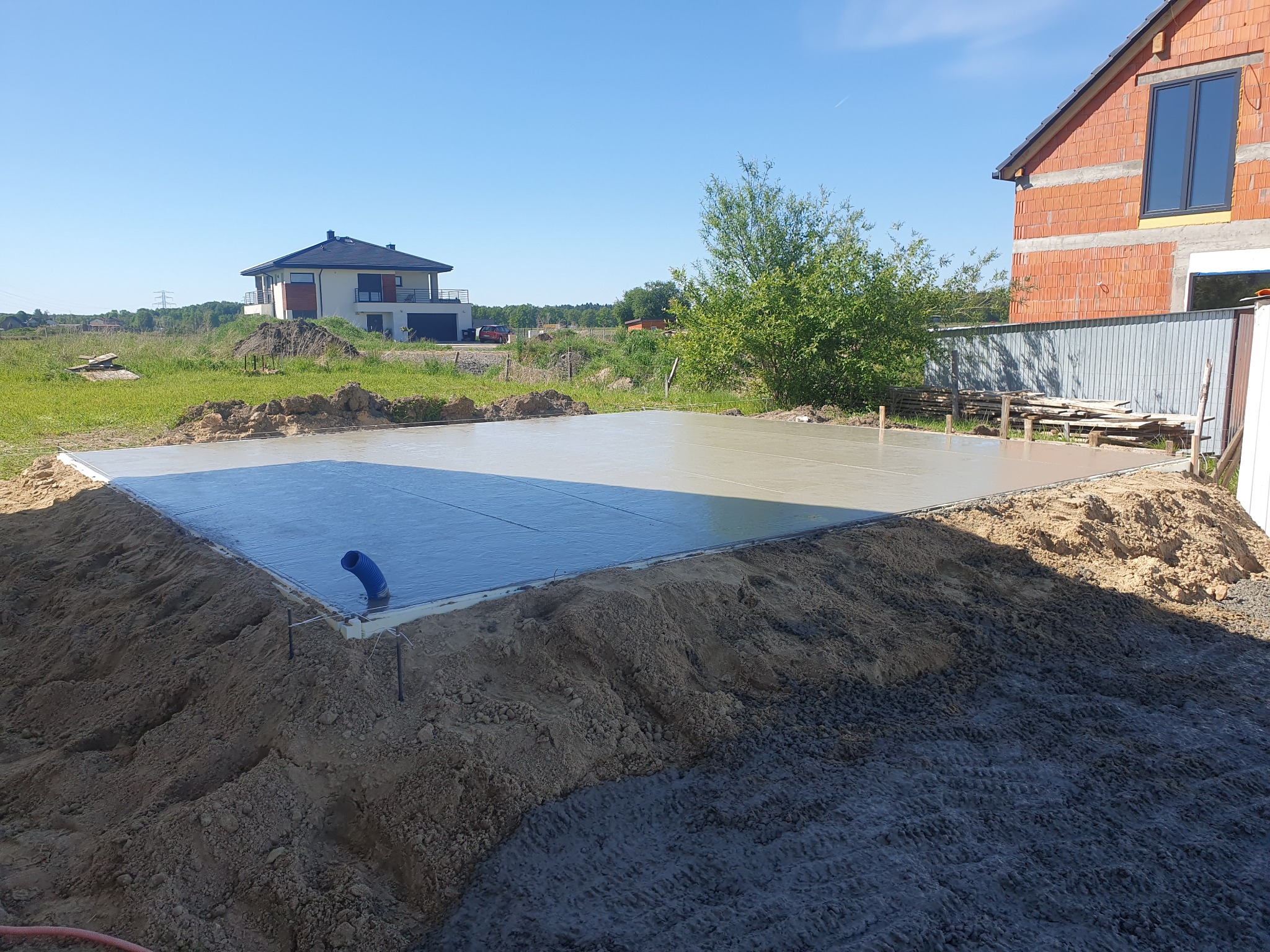 Wylana, świeża płyta betonowa fundamentowa pod budowę domu jednorodzinnego, widoczny niebieski przewód instalacyjny i otaczający grunt.
