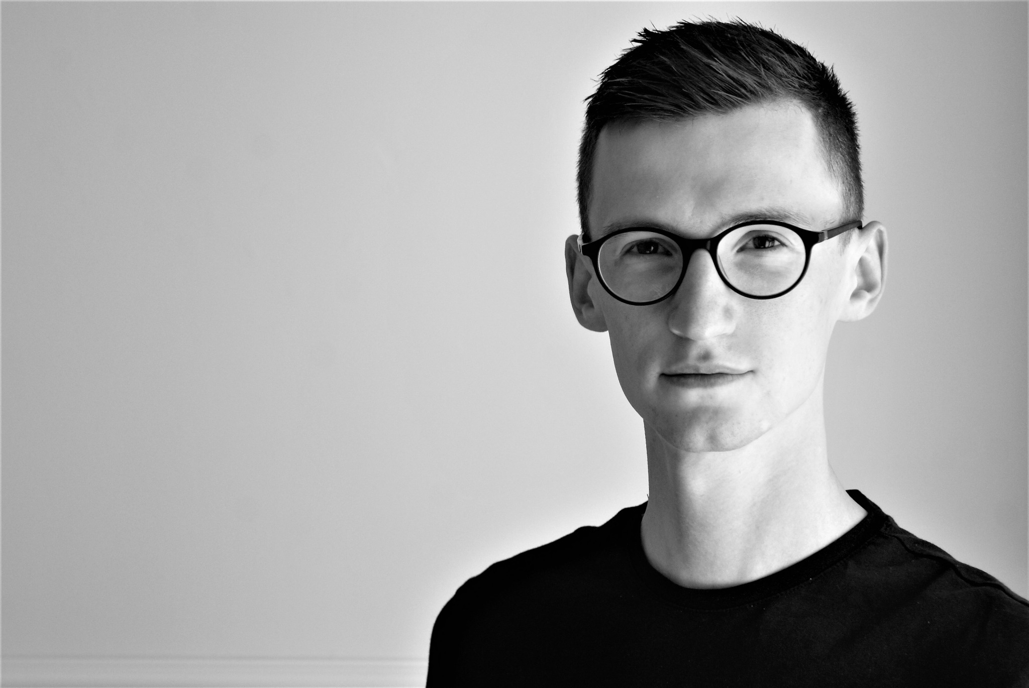 Portret młodego mężczyzny w okularach, czarno-białe zdjęcie z gładkim tłem.