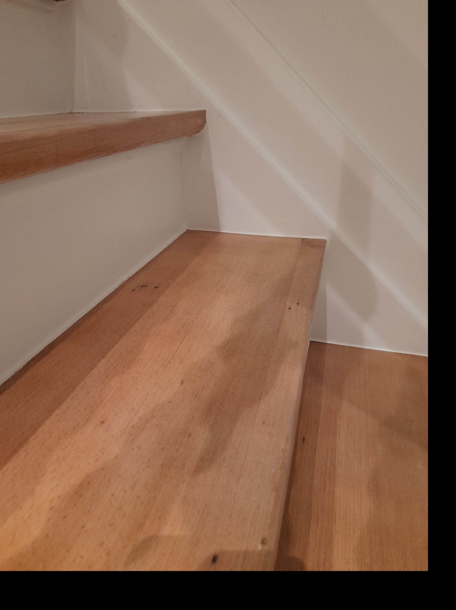 Fragment drewnianych schodów z białymi ścianami, widoczne niedoskonałości w wykończeniu spoin.