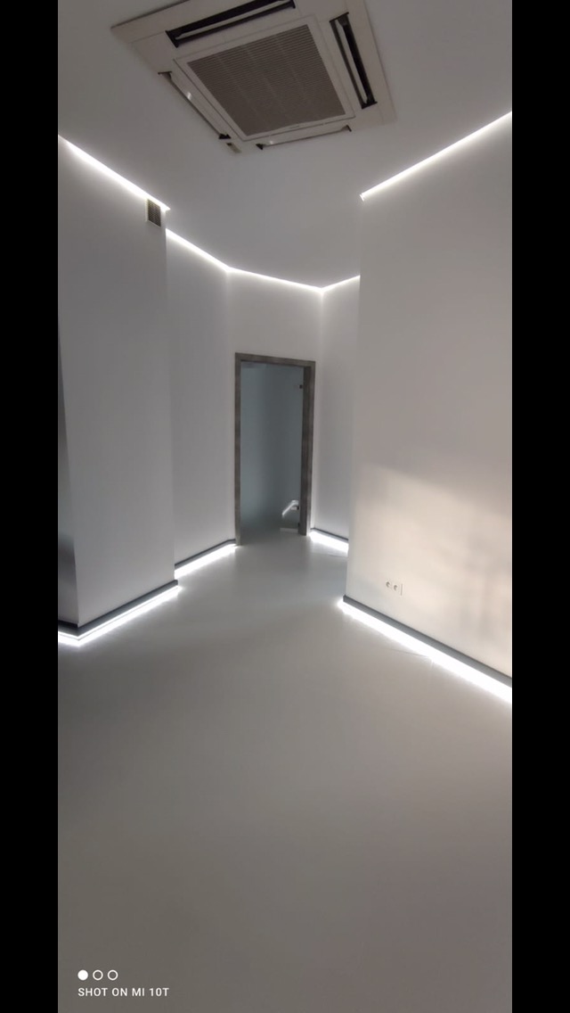 Nowoczesne wnętrze z białymi ścianami, podświetleniem LED przy podłodze i suficie oraz klimatyzacją kasetonową, widok na otwarte drzwi.