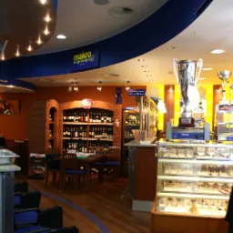 Wnętrze restauracji Makro Centrum HoReCa z ekspozycją win w regale z cegły, stołem z krzesłami oraz witryną chłodniczą na szkło, widoczny także kucharz z boku w uniformie i wysokiej czapce...