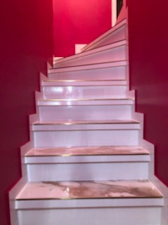 Białe, kręcone schody z marmurowymi stopniami i złotymi akcentami na tle intensywnie czerwonej ściany w Krakowie.