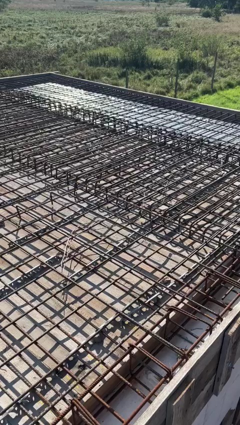 Zbrojenie płyty fundamentowej z widocznym deskowaniem i otaczającym terenem zielonym w tle.