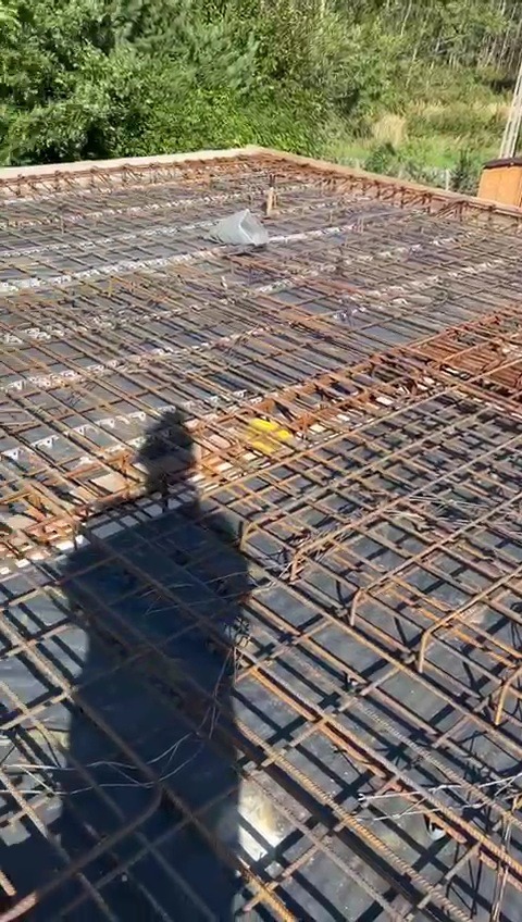 Zbrojenie stropu z widoczną siatką z prętów stalowych, ułożoną na czarnej folii, z perspektywy z góry, cień osoby w rogu kadru.