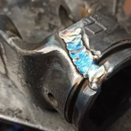 Spoina na elemencie metalowym z widocznymi kolorami utleniania, wykonana na warsztatowym stole.