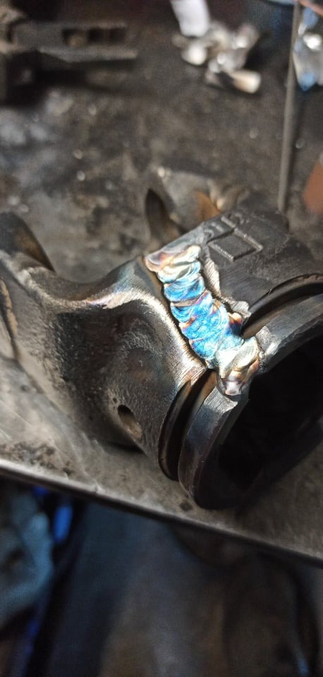 Spoina na elemencie metalowym z widocznymi kolorami utleniania, wykonana na warsztatowym stole.