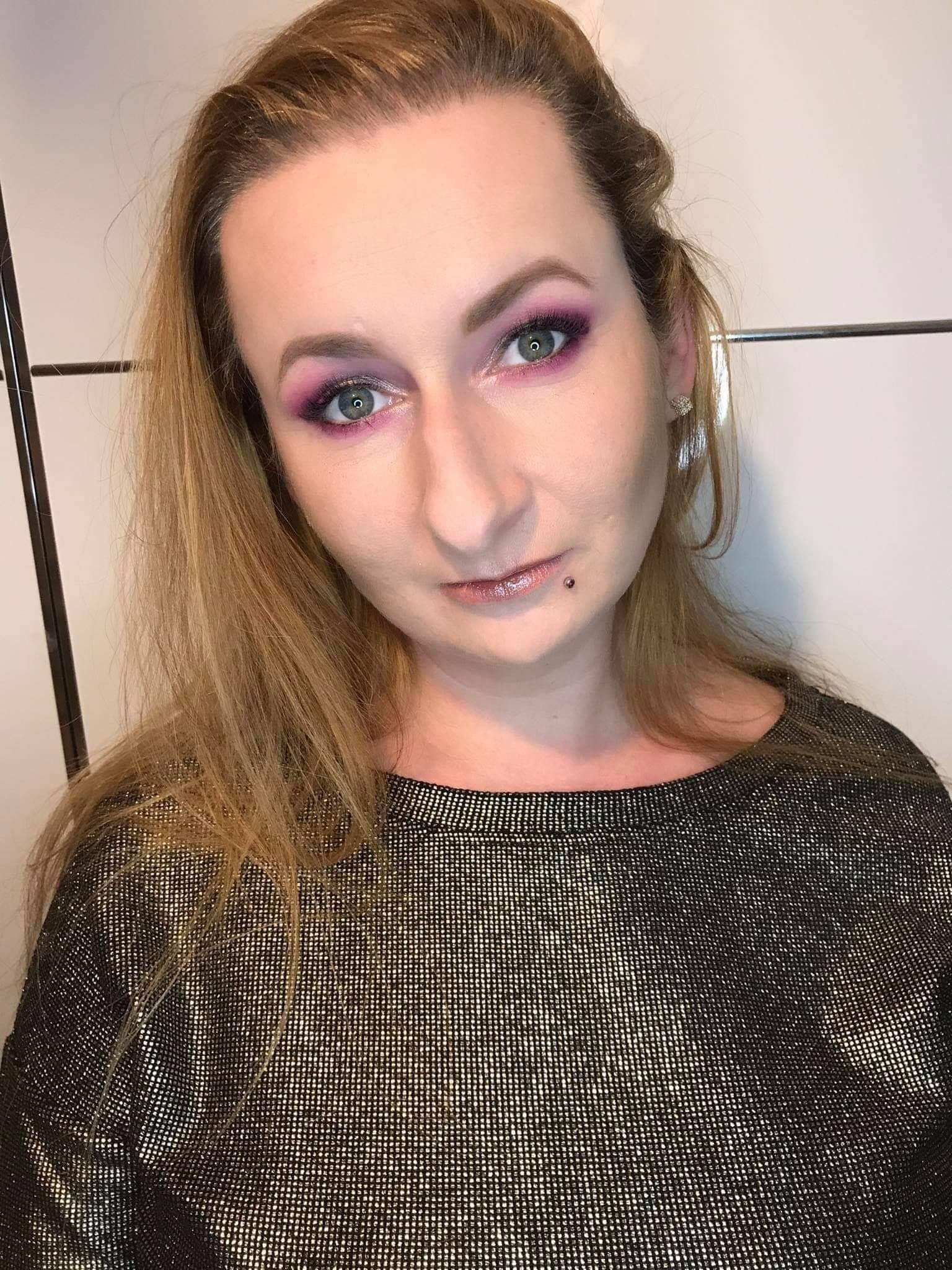 Portret kobiety z intensywnym, różowym cieniem na powiekach i błyszczącymi ustami, widoczny piercing nad ustami.