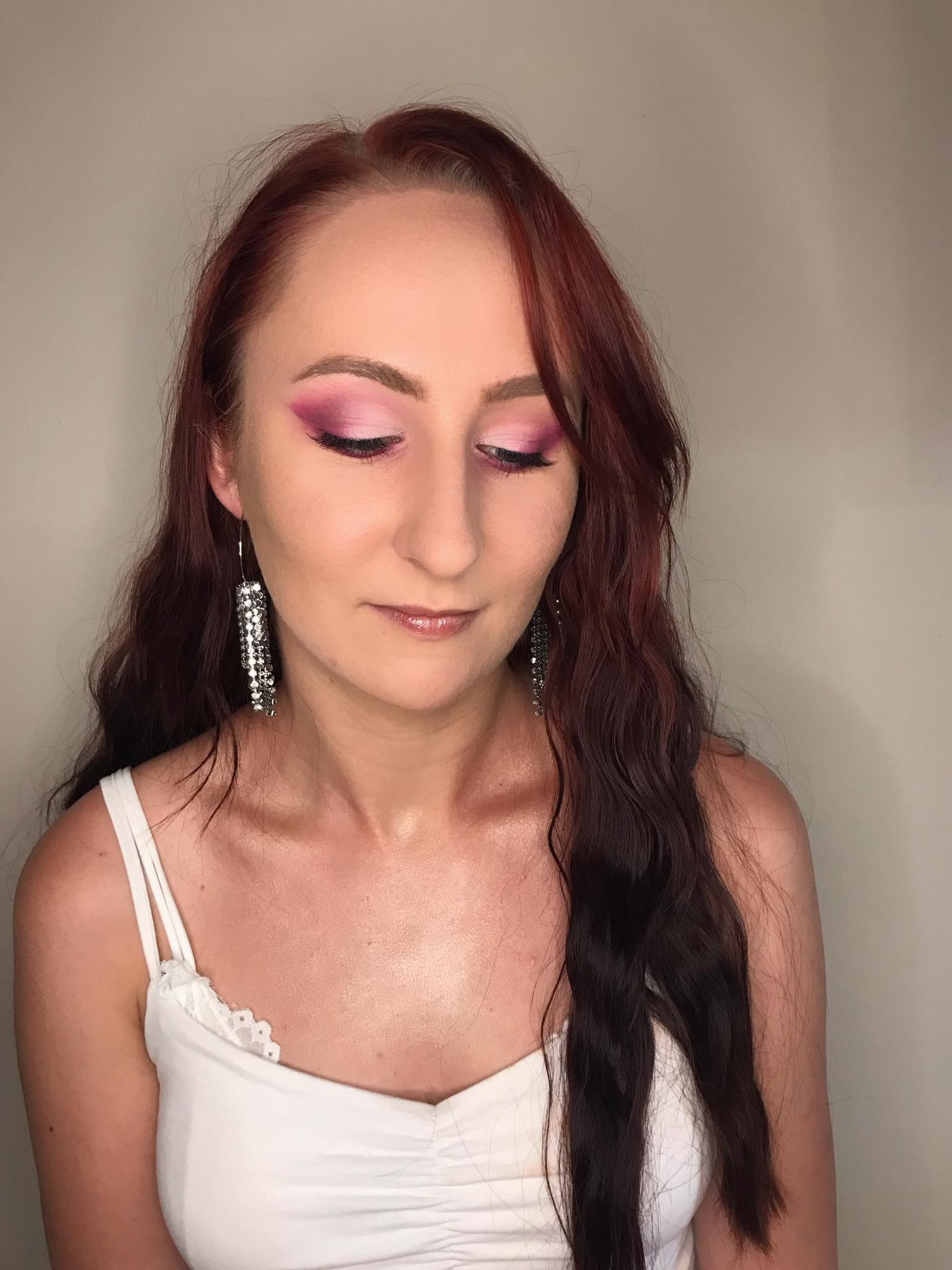 Kobieta z intensywnym różowym makijażem oczu, długimi, rudymi włosami i błyszczącymi, kaskadowymi kolczykami.