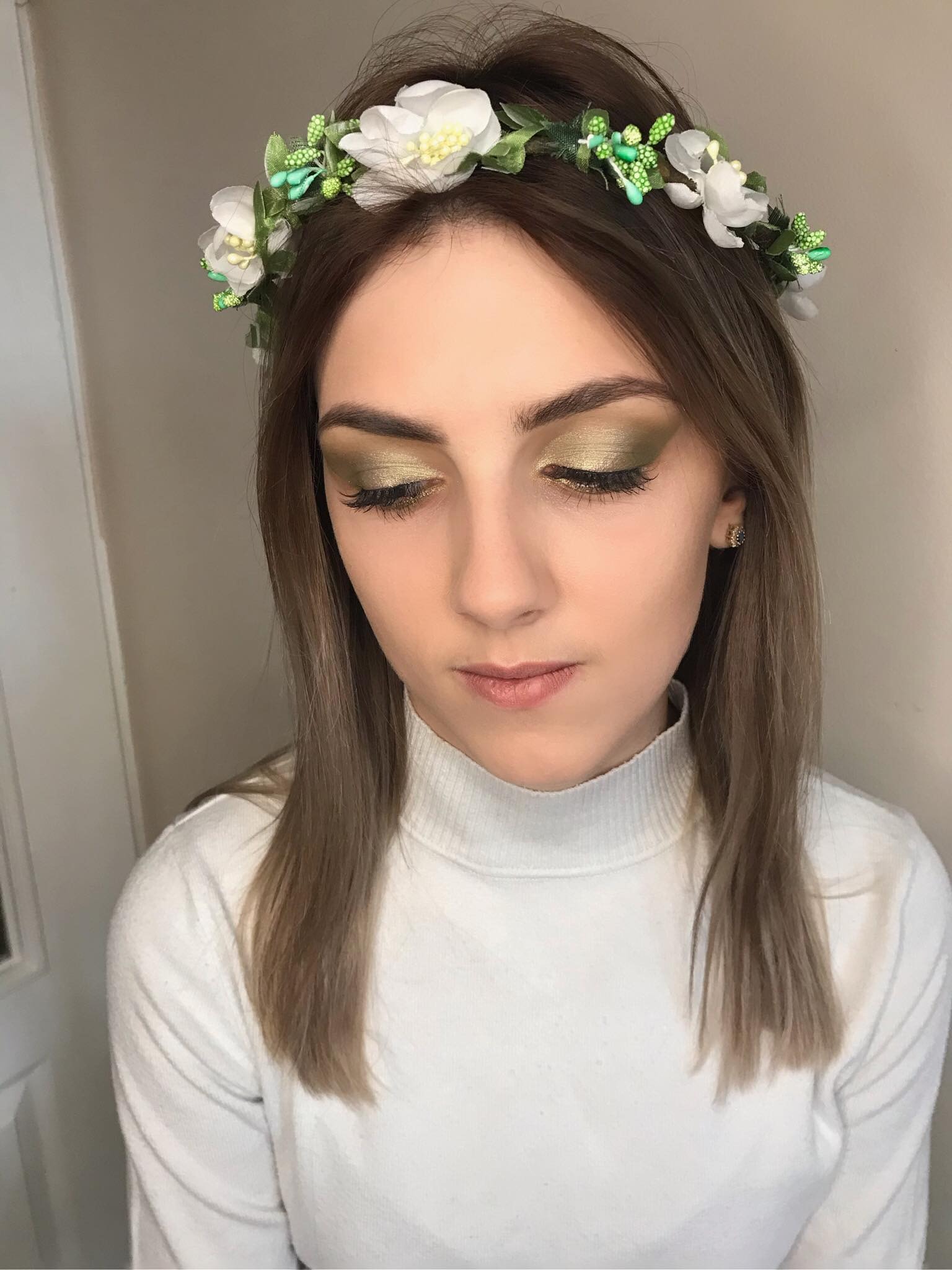 Portret kobiety z zielonym cieniem na powiekach i wiankiem z białych kwiatów na głowie, spuszczony wzrok.