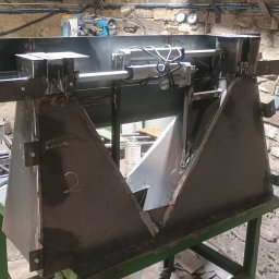 Krzysztof Orłowski - Konstrukcja z surowej stali z siłownikami pneumatycznymi, spawana w warsztacie, obok spawarka Magnum MIG220 MMA, na tle murowanej ściany.