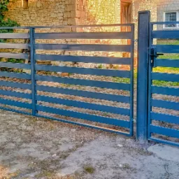 Nowoczesna, pozioma brama wjazdowa z metalu w kolorze grafitowym. Widoczne poziome profile i solidne słupki. Tło stanowi budynek z kamienia i zieleń.