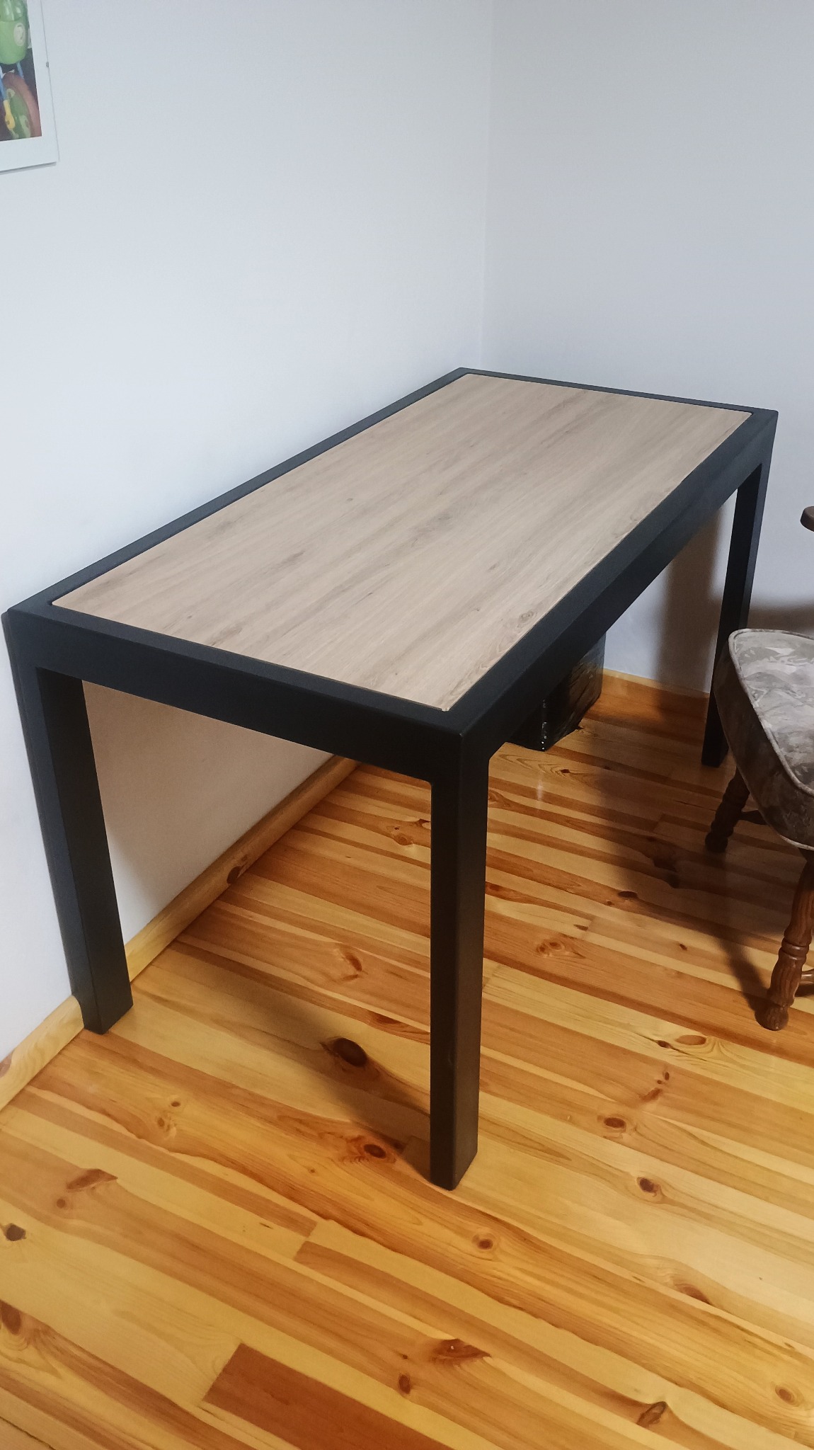 Stół z blatem imitującym drewno i czarnymi, metalowymi nogami. Minimalistyczny design, widoczna struktura drewna na blacie i solidne wykonanie.