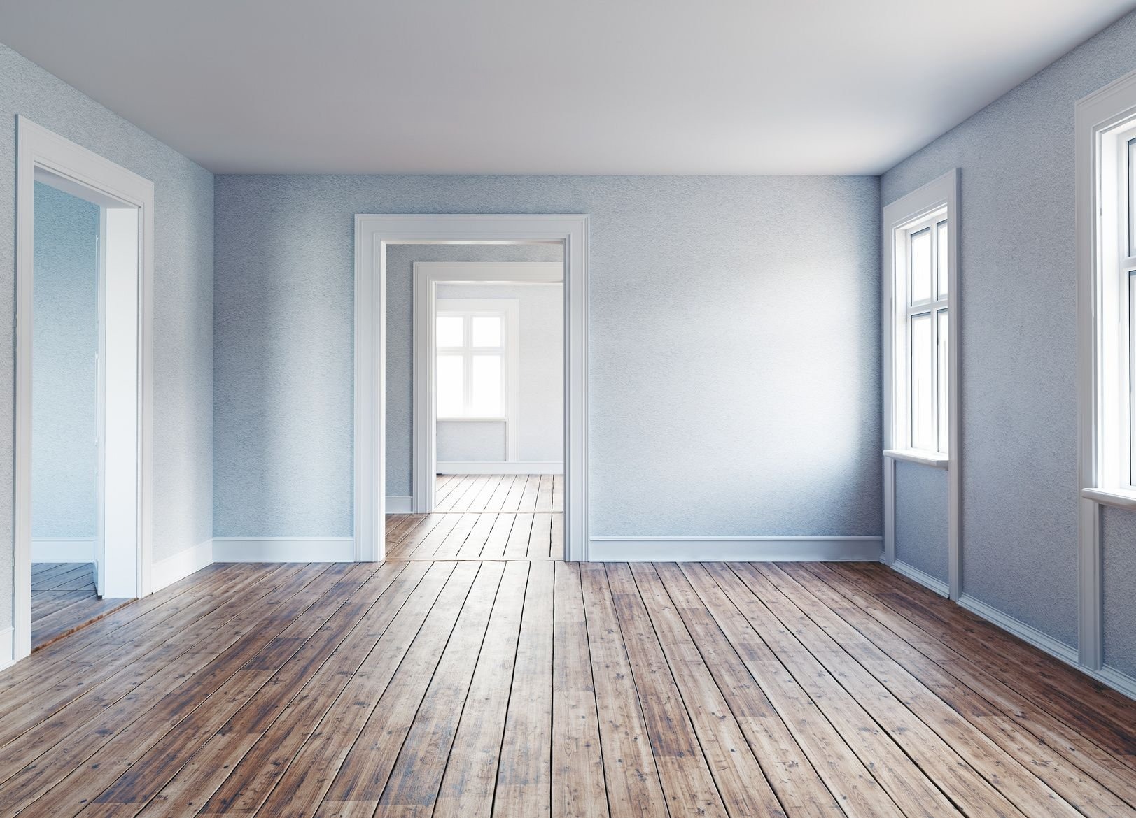 Pusty pokój z drewnianą podłogą, świeżo pomalowanymi ścianami o delikatnej fakturze i białymi listwami przypodłogowymi, widoczne trzy pary drzwi prowadzące do kolejnych pomieszczeń z oknami.