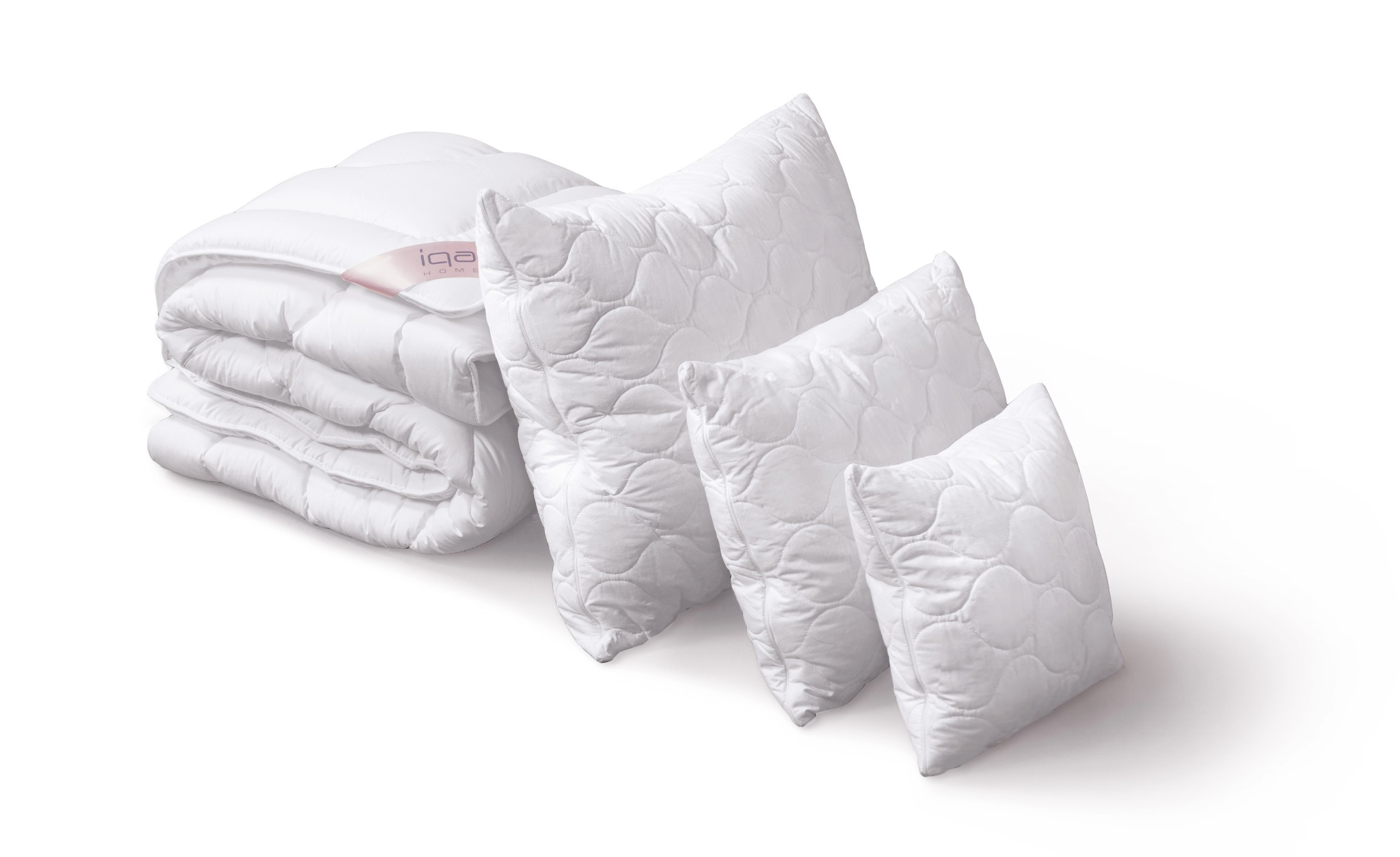 Stos białej kołdry z różową etykietą marki oraz trzy białe poduszki z pikowaniem w kształcie kół na białym tle.