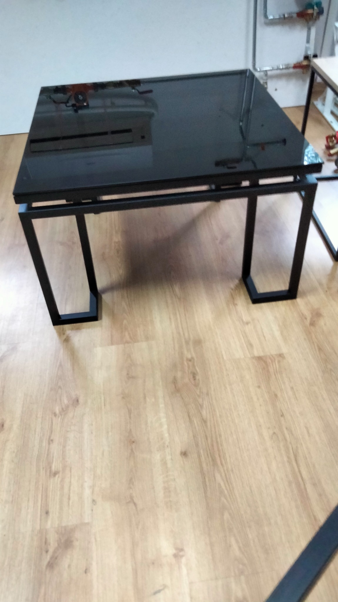 Stolik kawowy z czarnym, metalowym stelażem i szklanym blatem na drewnianej podłodze.