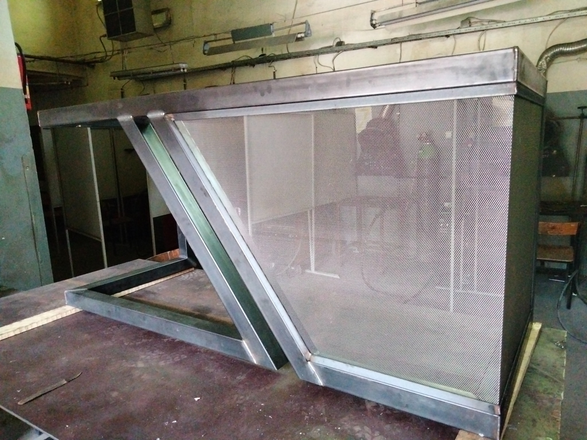 Metalowa konstrukcja z perforowanej blachy, spawana z profili, ustawiona w warsztacie na stole roboczym.