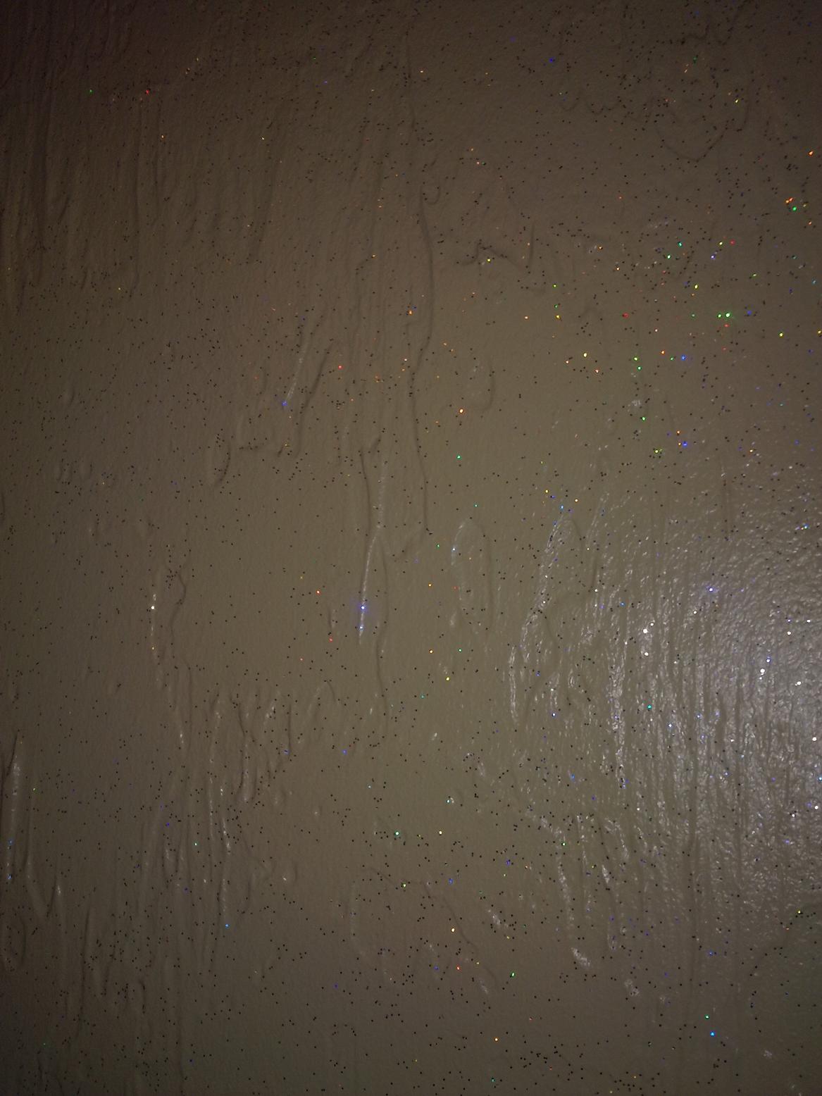 Tekstura ściany z efektem brokatu i nierównomierną fakturą, oświetlona z góry, w odcieniach beżu i szarości.