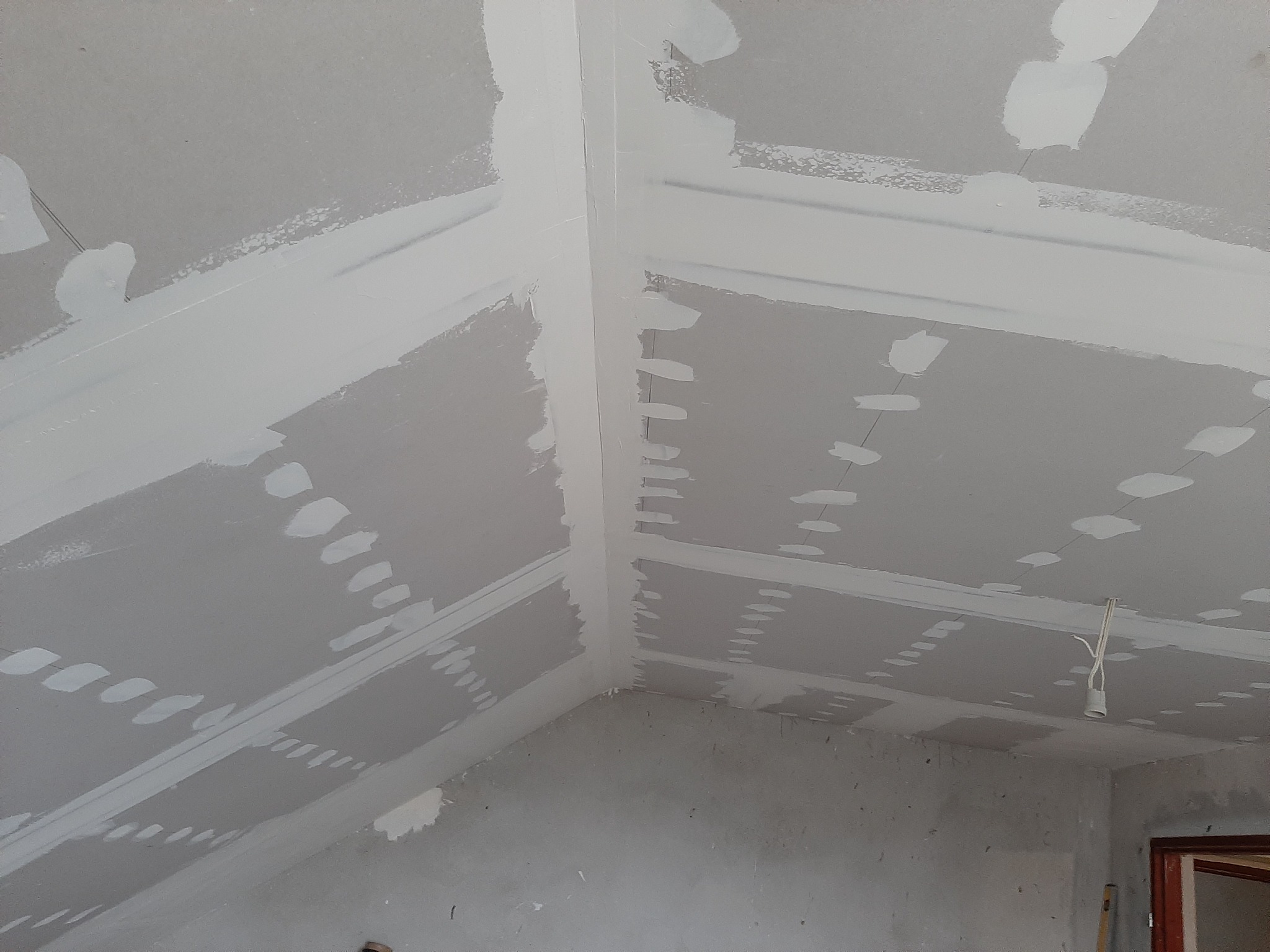 Poddasze w trakcie wykańczania: płyty gipsowo-kartonowe na skosach, widoczne łączenia szpachlowane, surowa instalacja elektryczna zwisająca z sufitu, fragment ościeżnicy drzwiowej w tle.