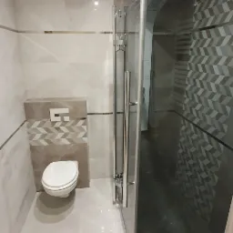 Łazienka z płytkami gresowymi z połyskiem, zabudowa geberit oraz kabina szklana, brodzik obłożony płytkami.