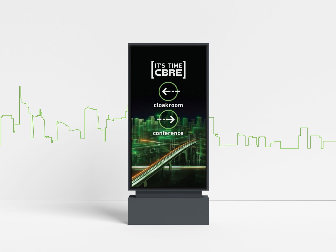 Cyfrowy szyld informacyjny z logo CBRE i strzałkami wskazującymi kierunek do szatni i sali konferencyjnej, na tle neonowej panoramy miasta.