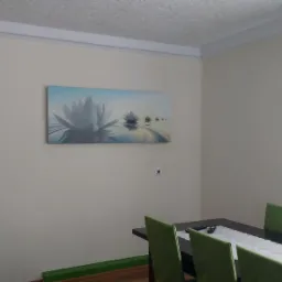 Jasne wnętrze pokoju z obrazem lotosów nad stołem jadalnym i zielonymi krzesłami, oświetlone naturalnym światłem zza zielonych zasłon.