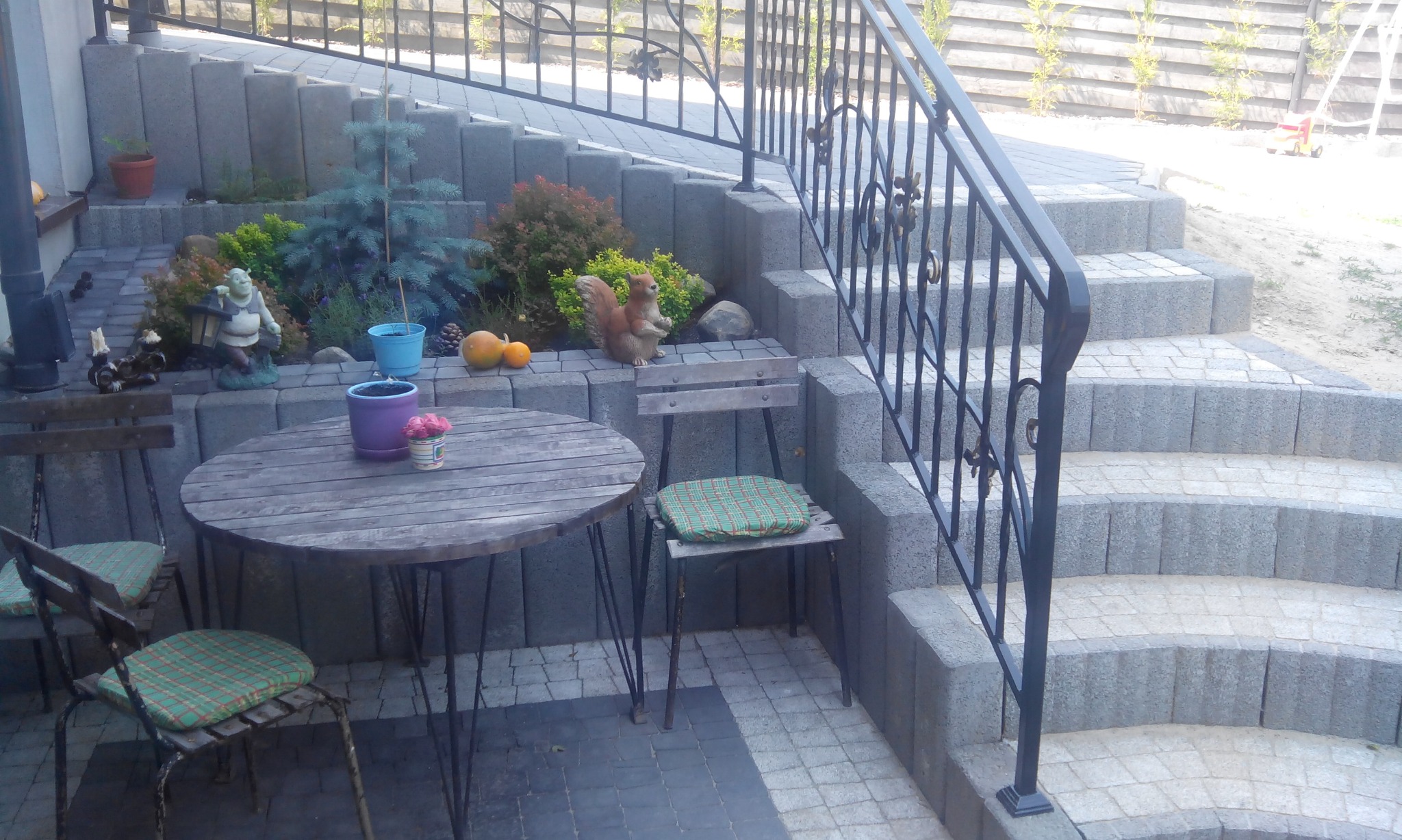 Kostka brukowa Arko ułożona na tarasie i schodach, z obrzeżami Palinea i palisadą Zen, oraz rustykalnym stolikiem i krzesłami w tle.