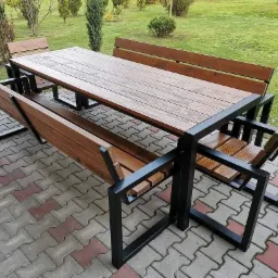 Stół piknikowy z drewna i metalu z dwiema ławkami i dwoma krzesłami w nowoczesnym stylu, ustawiony na brukowanym patio z trawnikiem w tle.