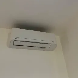 Biała jednostka klimatyzacji Toshiba zamontowana na jasnej ścianie, widok z dołu.