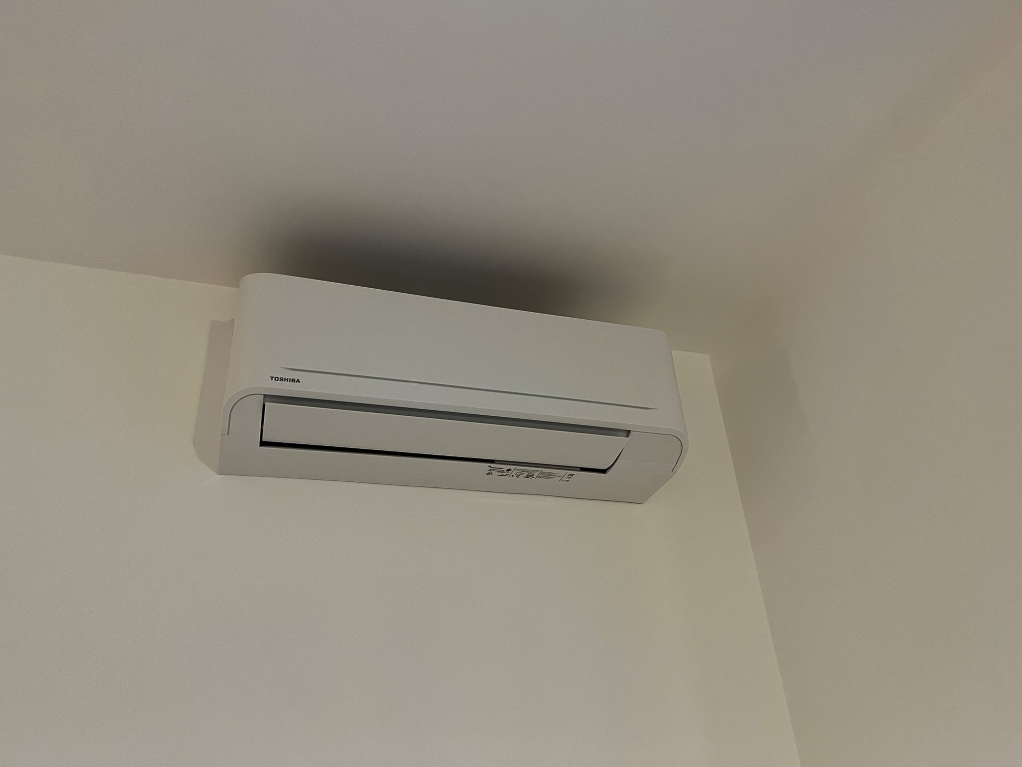 Biała jednostka klimatyzacji Toshiba zamontowana na jasnej ścianie, widok z dołu.