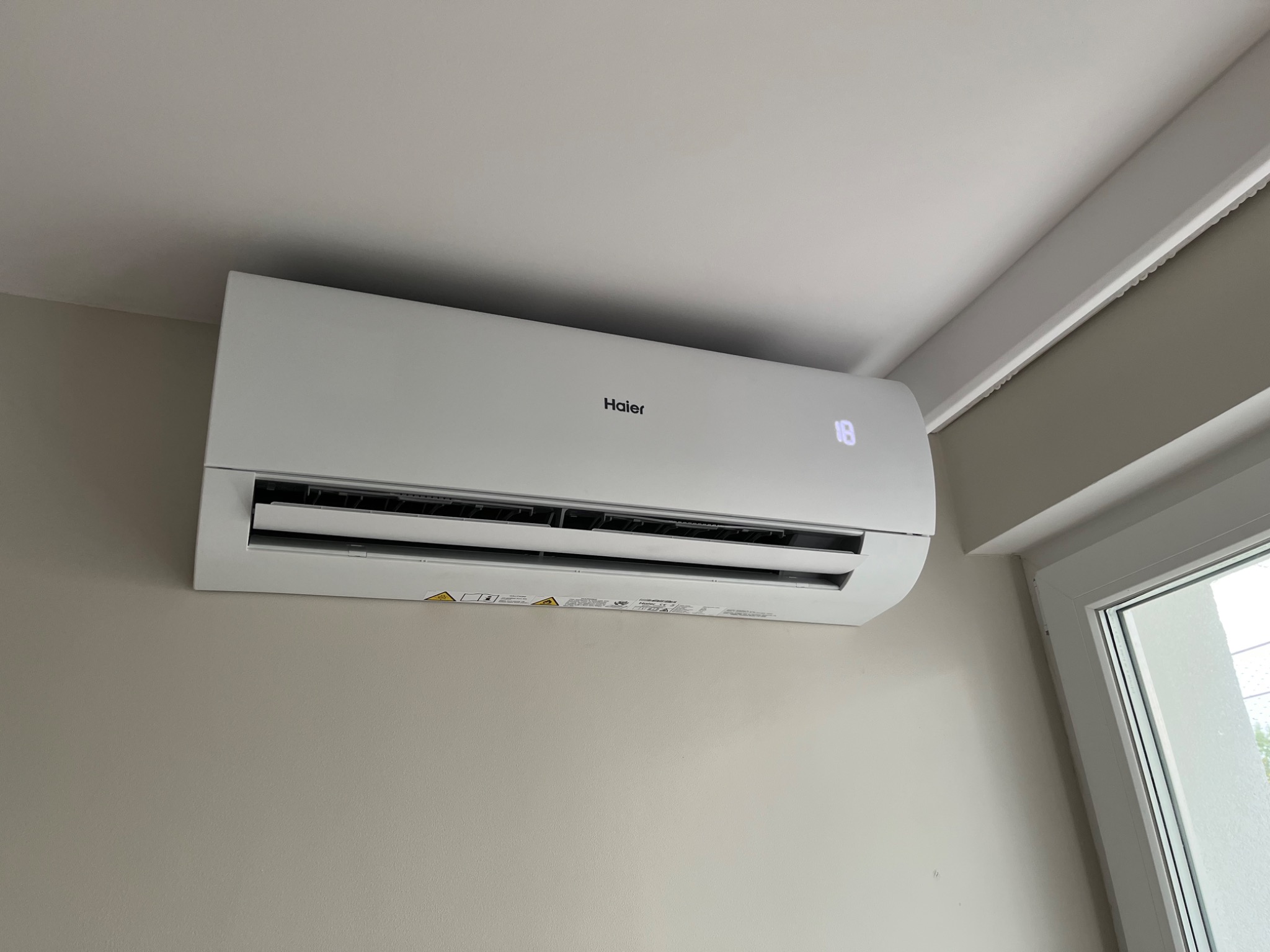 Klimatyzator Haier zamontowany na ścianie w domu w Nadarzynie, ustawiony na temperaturę 18 stopni, widoczny fragment okna.