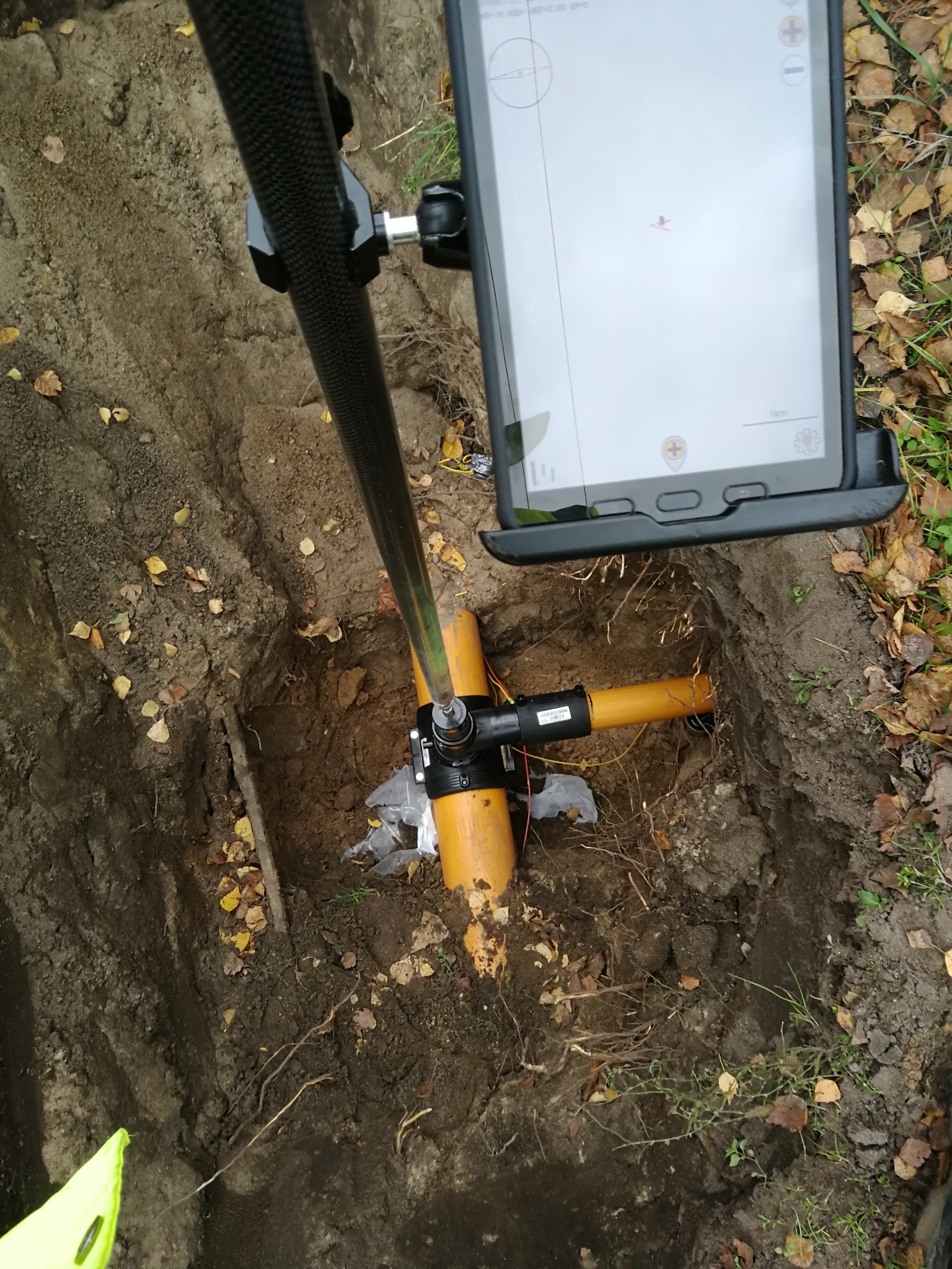 Orange rury w wykopie, widok z góry z tabletem wskazującym lokalizację, jesienne liście wokół.