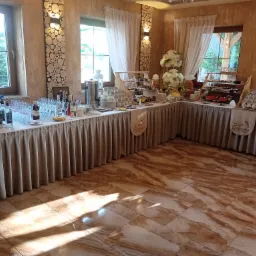 Stół cateringowy z deserami, napojami i kwiatami na sali bankietowej z oknami i drewnianymi dekoracjami ściennymi.