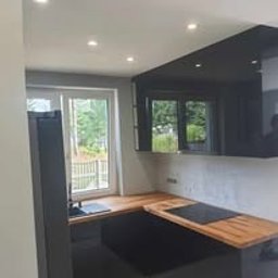 Fabryka Snów Adam Pawlicki - Czarna, lakierowana kuchnia z drewnianym blatem, widok na zewnątrz przez okno. Minimalistyczny design, oświetlenie punktowe sufitowe.