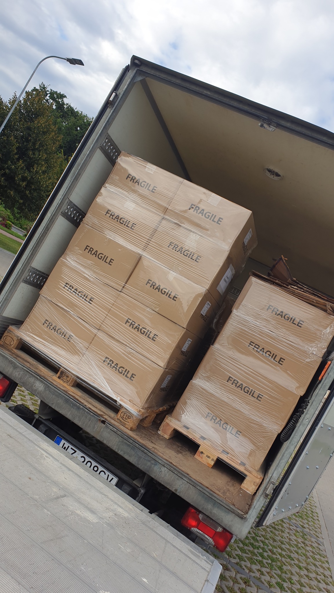 Wnętrze busa transportowego z załadowanymi paletami kartonów oznaczonych napisem 'FRAGILE', zabezpieczonych folią stretch.