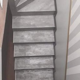 Michał Kukawa - Betonowe schody w nowoczesnym stylu, z widoczną ścianą w biało-szare pasy, uchwycone z perspektywy góry.