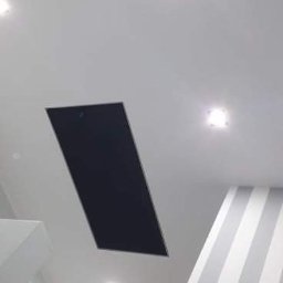 Michał Kukawa - Biały sufit z czarnym panelem rewizyjnym, oświetleniem punktowym LED i fragmentem ściany w biało-szare pasy w nowoczesnym wnętrzu.