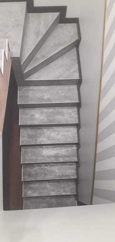 Betonowe schody w nowoczesnym stylu, z widoczną ścianą w biało-szare pasy, uchwycone z perspektywy góry.