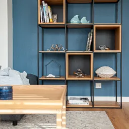 Nowoczesny regał z drewnianymi półkami i metalową konstrukcją, z dekoracjami takimi jak ceramiczne figurki ptaków, metalowa rzeźba ośmiornicy, książki i ozdobne naczynia, ustawiony na tle...