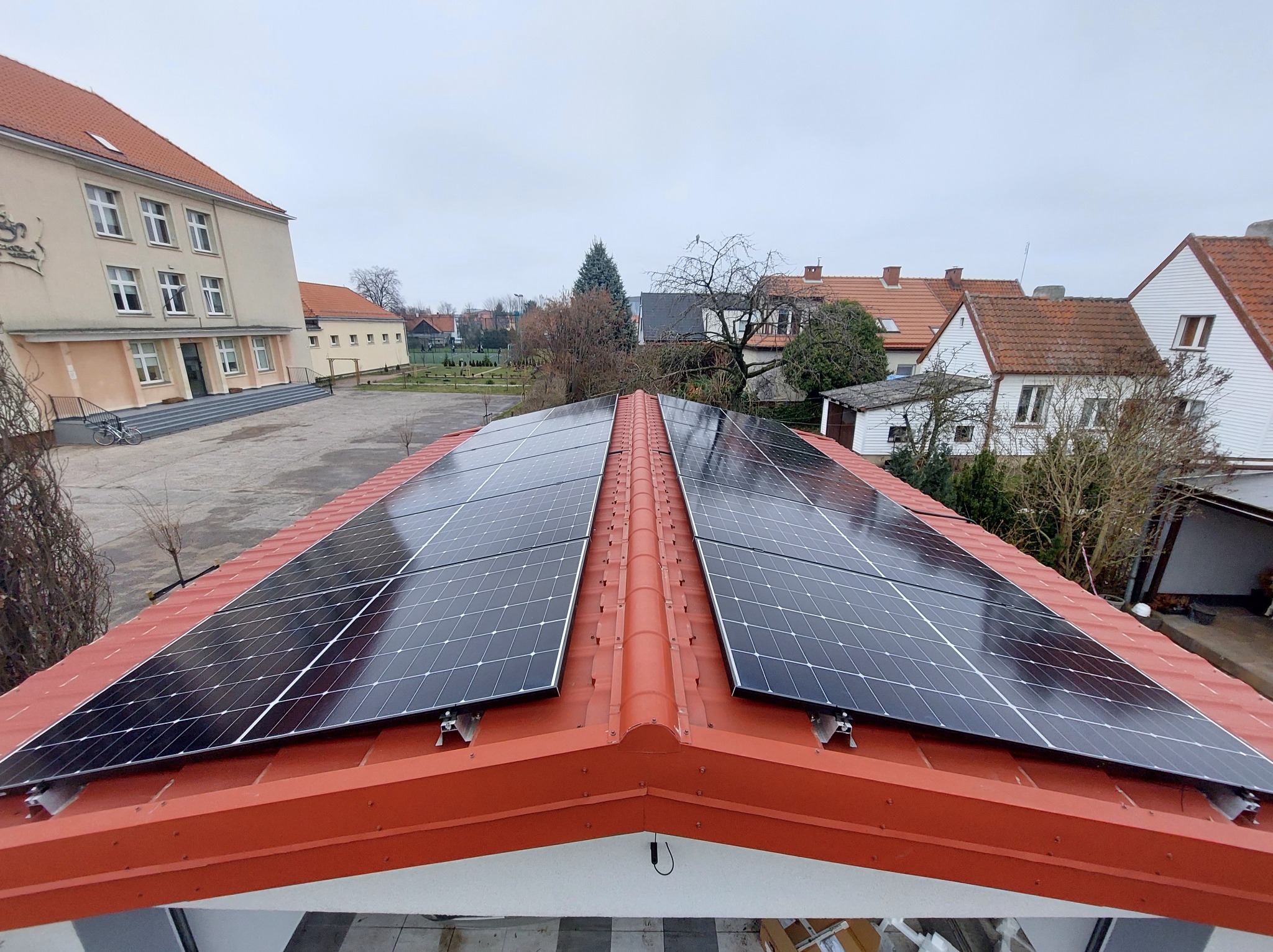 Panele fotowoltaiczne na czerwonym dachu budynku z widokiem na okolicę. Montaż paneli słonecznych na dachu.