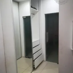 Nowoczesna szafa wnękowa z przesuwnymi lustrzanymi drzwiami, widoczne otwarte szuflady i półki, logo firmy w prawym górnym rogu.