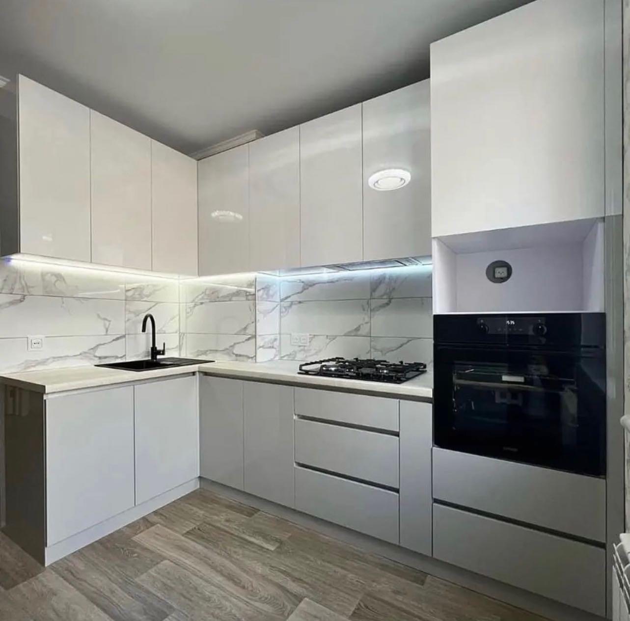 Nowoczesna kuchnia w odcieniach bieli i szarości z błyszczącymi frontami szafek, marmurowym wzorem na ścianie nad blatem i czarną armaturą oraz płytą gazową.