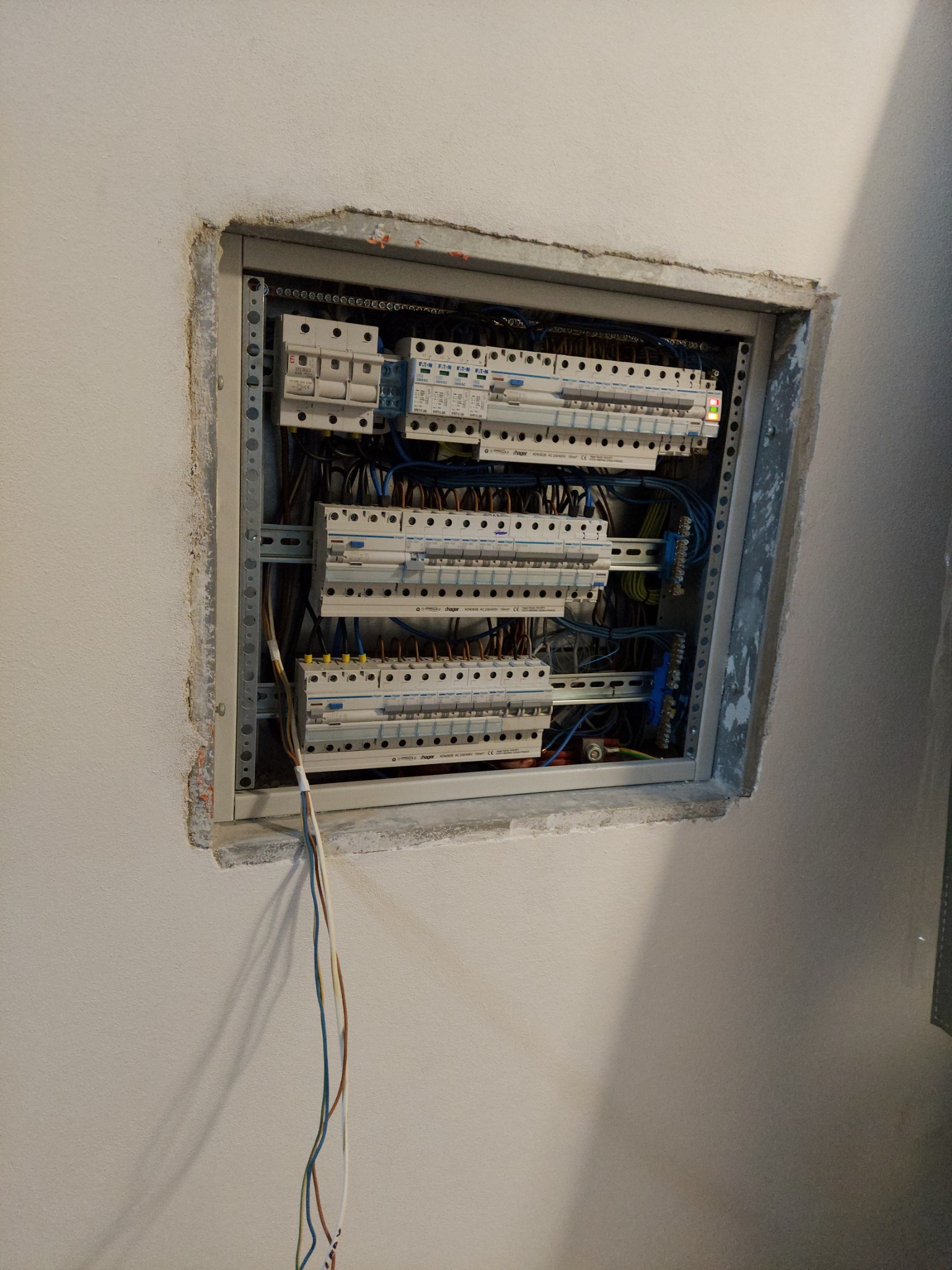 Tablica rozdzielcza z zamontowanymi bezpiecznikami i okablowaniem, umieszczona we wnęce w ścianie podczas prac instalacyjnych w Gliwicach. Widoczne wystające przewody elektryczne.