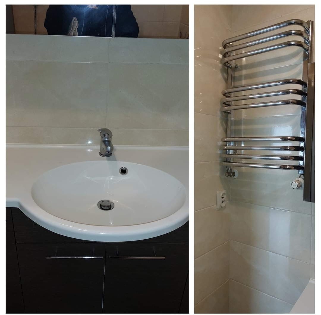 Umywalka ceramiczna z szafką w kolorze ciemnego drewna i chromowaną baterią, obok grzejnik drabinkowy w łazience wykończonej beżowymi płytkami.